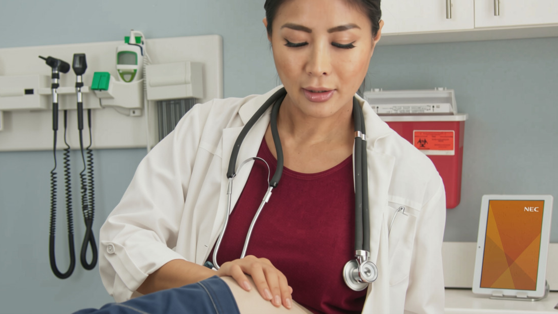 Clinician performing a physical assessment on a patient's knee in a medical examination room.