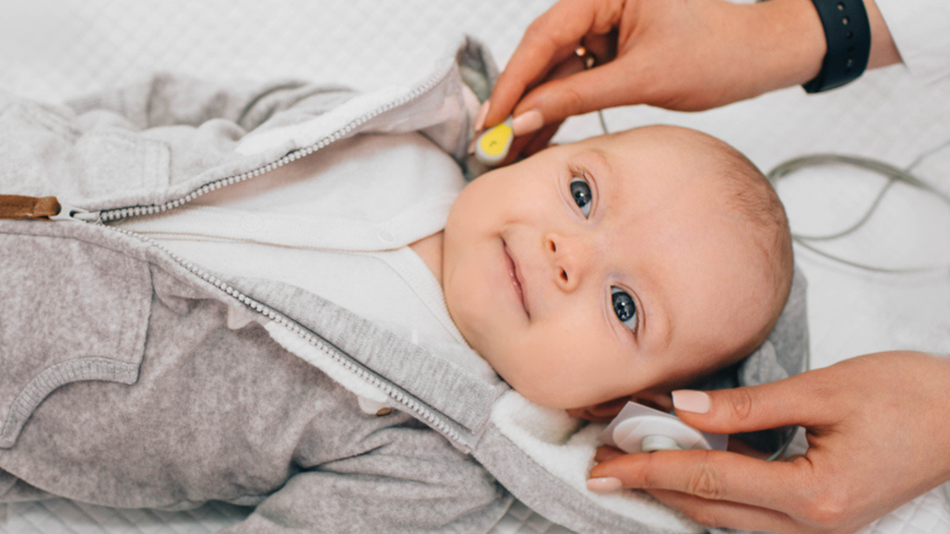 Infant undergoing routine newborn health screening with monitoring sensors attached.