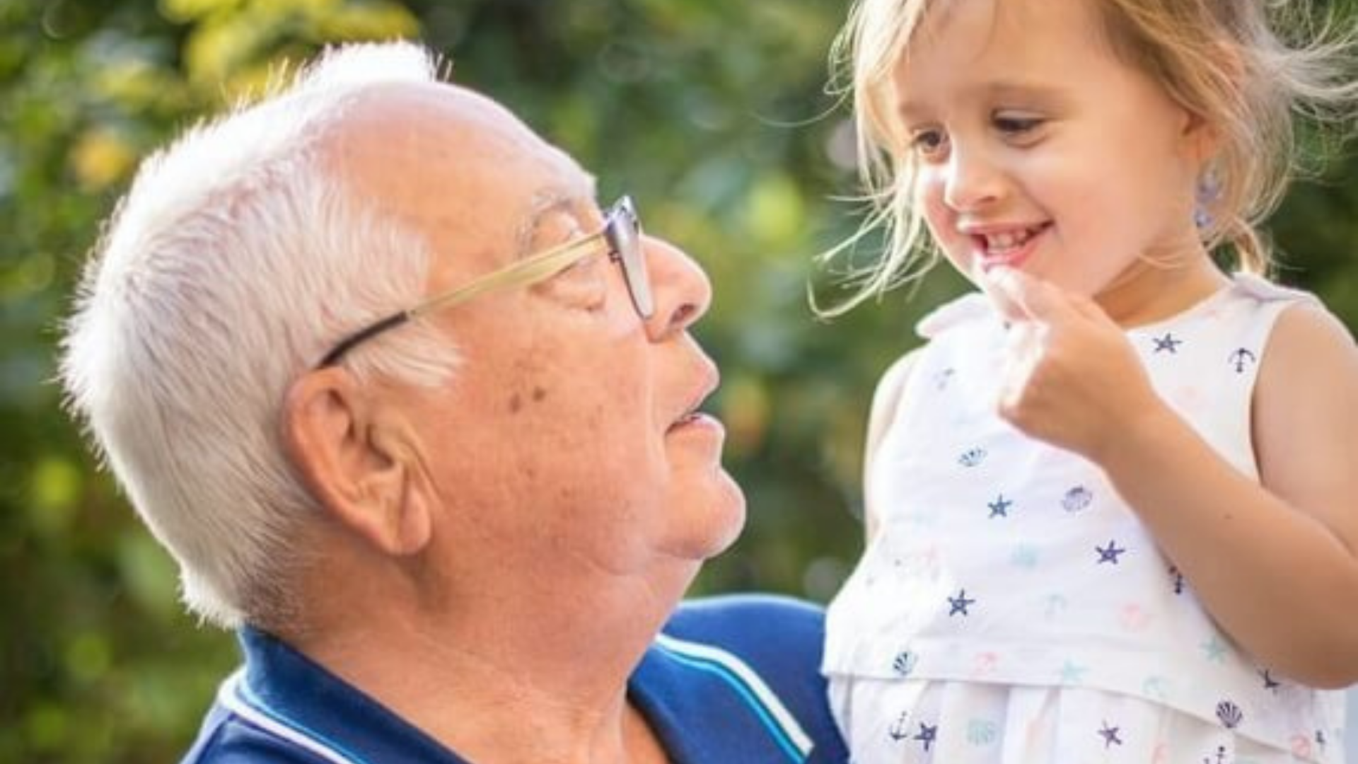 A Grandfather affectionately holding his Grandaughter in his arms whilst looking up at her