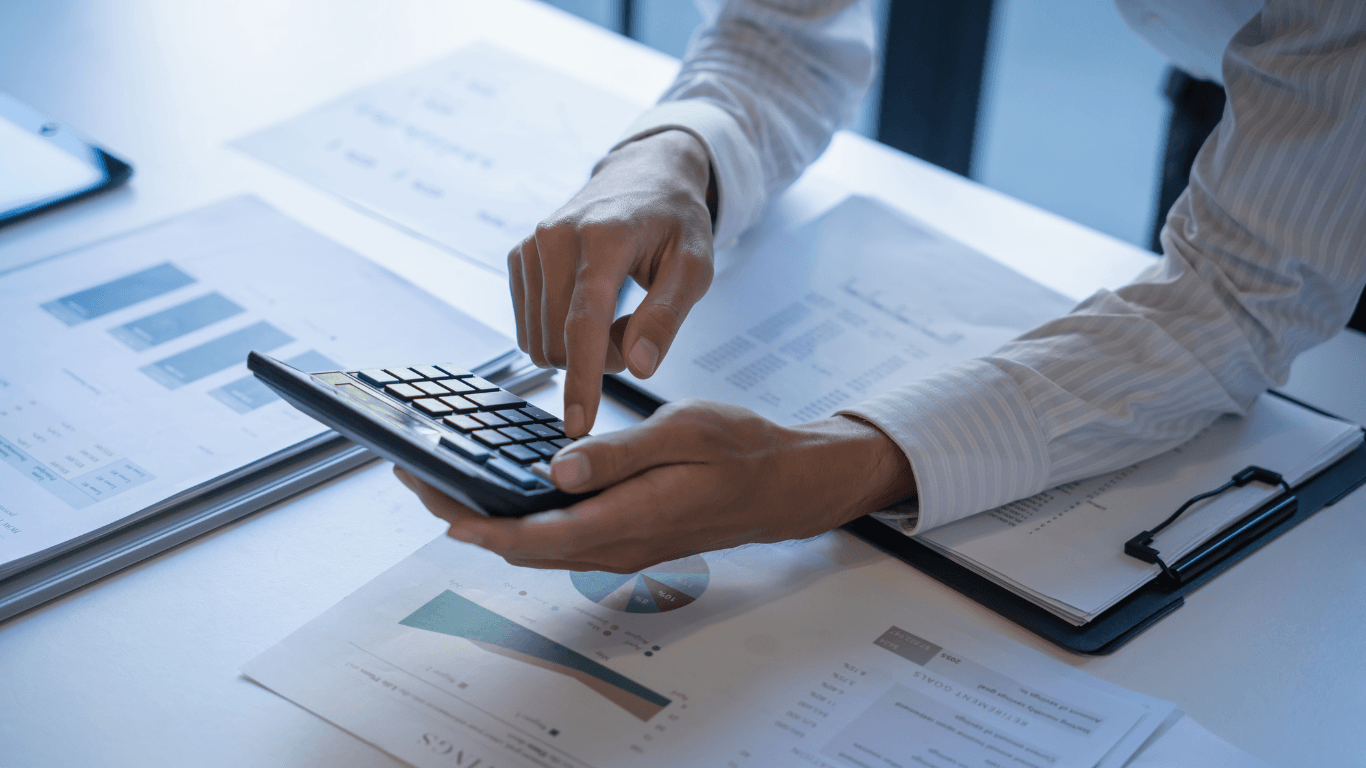 Close-up of hands using a calculator over financial reports and charts on a desk, reviewing budgets and business data.