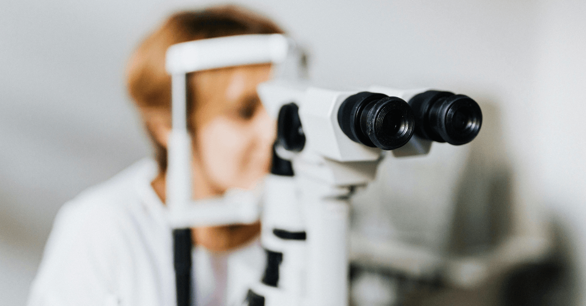 Close-up view of an eye examination microscope in focus, with a healthcare professional blurred in the background