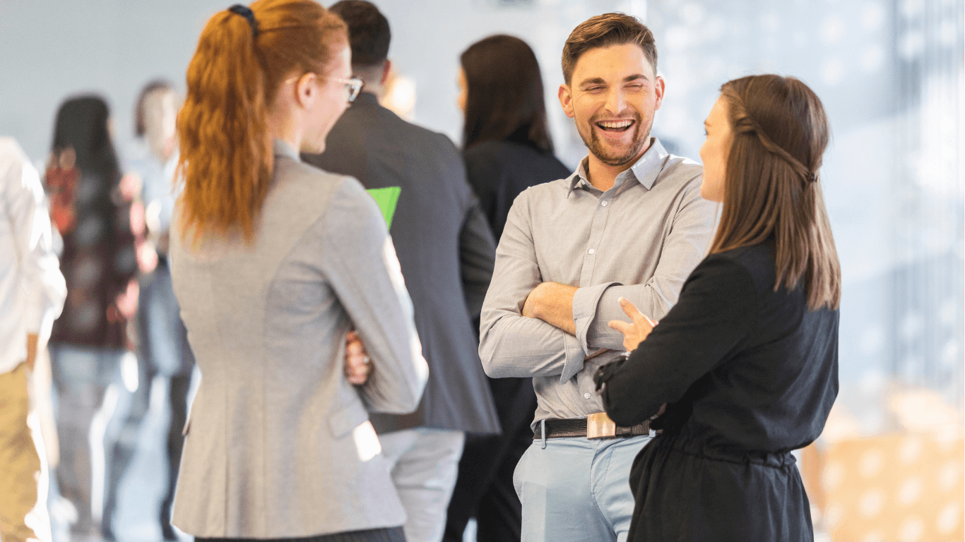 People networking at a business event, standing in small groups and talking in a bright, modern conference space indoors area.