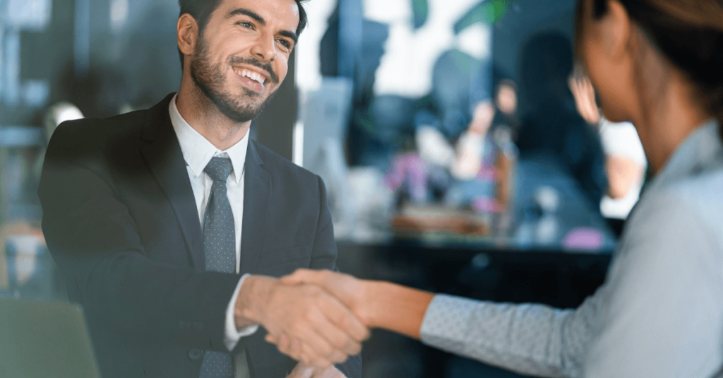 Two professionals shake hands across a meeting table, symbolising partnership, collaboration, and business success.