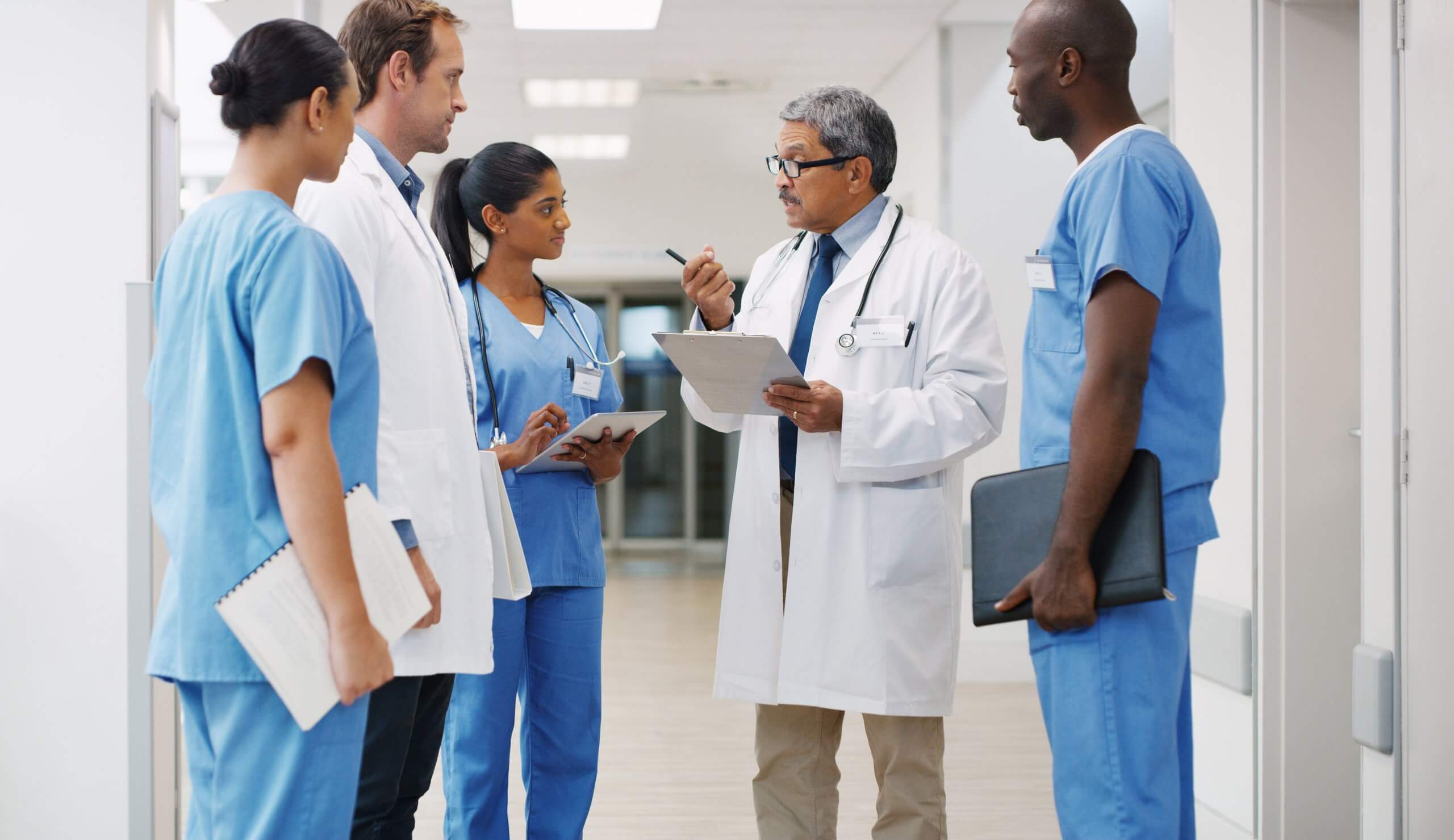 Healthcare team gathers in a hospital corridor as a senior clinician reviews notes and discusses patient care plans.