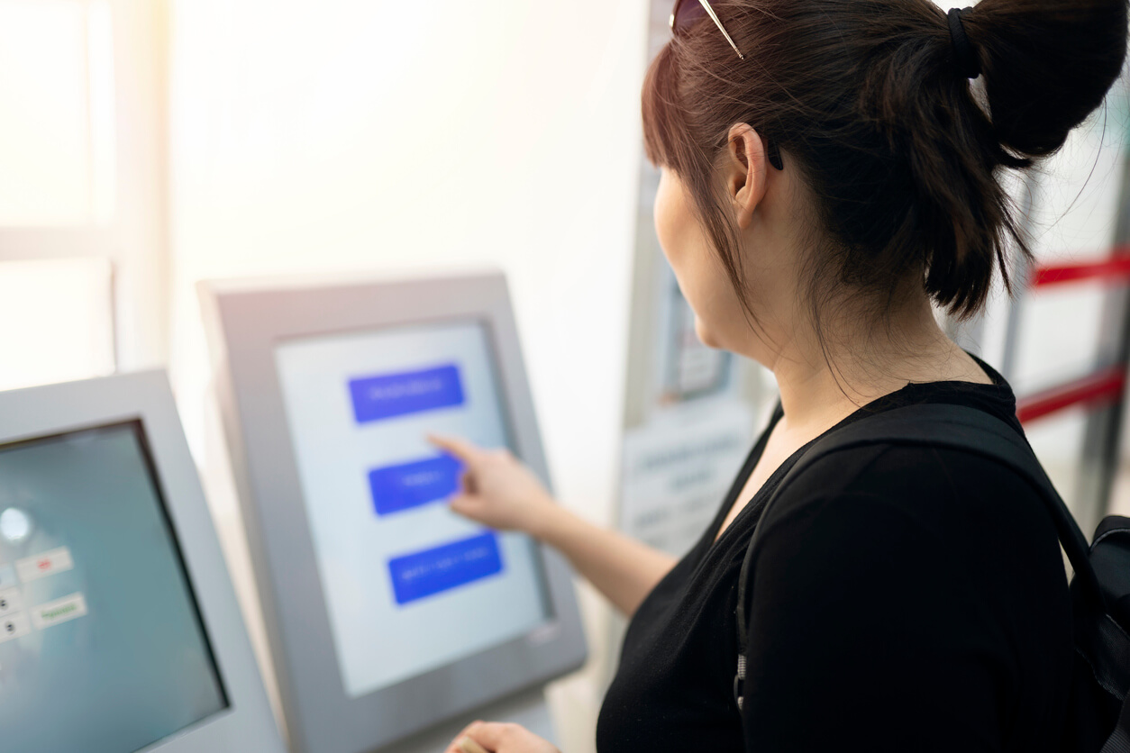 Person using a touchscreen terminal to access digital services, with menu options displayed on the screen in a public indoor setting.
