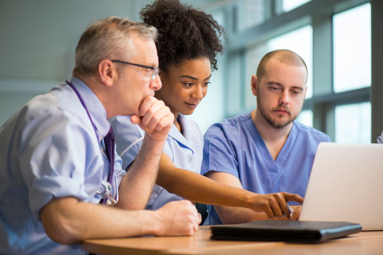 Healthcare team reviews information on a laptop during a collaborative meeting, discussing patient care and workflow.