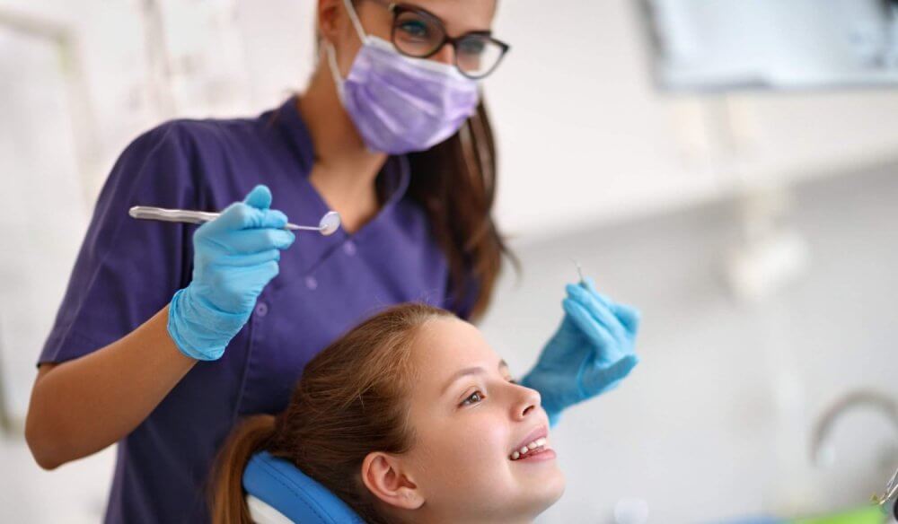 Dental professional wearing protective equipment preparing to examine a child seated in a dental chair during a routine dental appointment.
