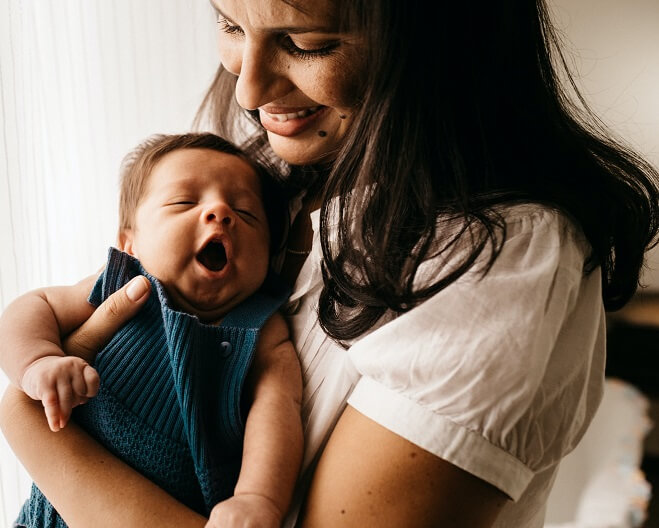 A close up view of a mother looking down and holding her sleeping baby in her arms